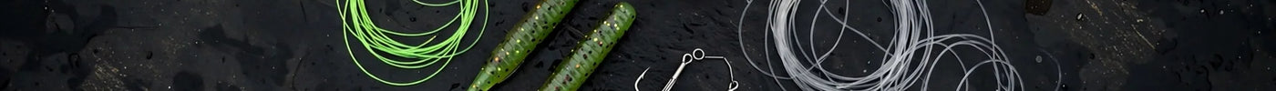 Fishing line spools, soft plastic stick worms, hooks and weights laid out on a dark boat deck
