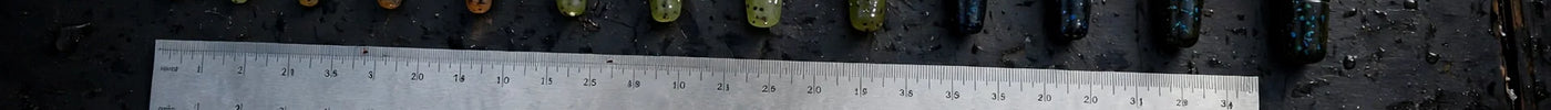 Soft plastic stick worms in graduated sizes with a ruler, hooks, weights, and pliers on a dark boat deck