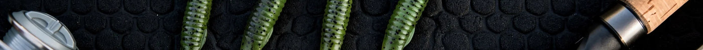 Ned rig tackle flat-lay: mushroom jig heads, finesse worms and hooks on a dark boat deck