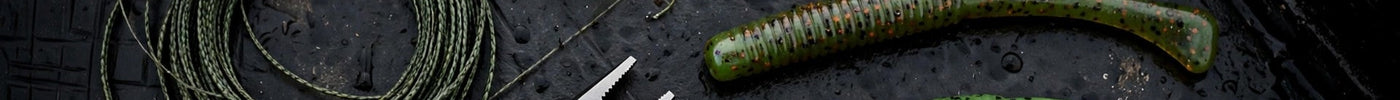 Texas rig tackle flat-lay on a dark boat deck: tungsten bullet weights, wide-gap worm hooks, braided line, pliers, stick worms, and milfoil sprigs