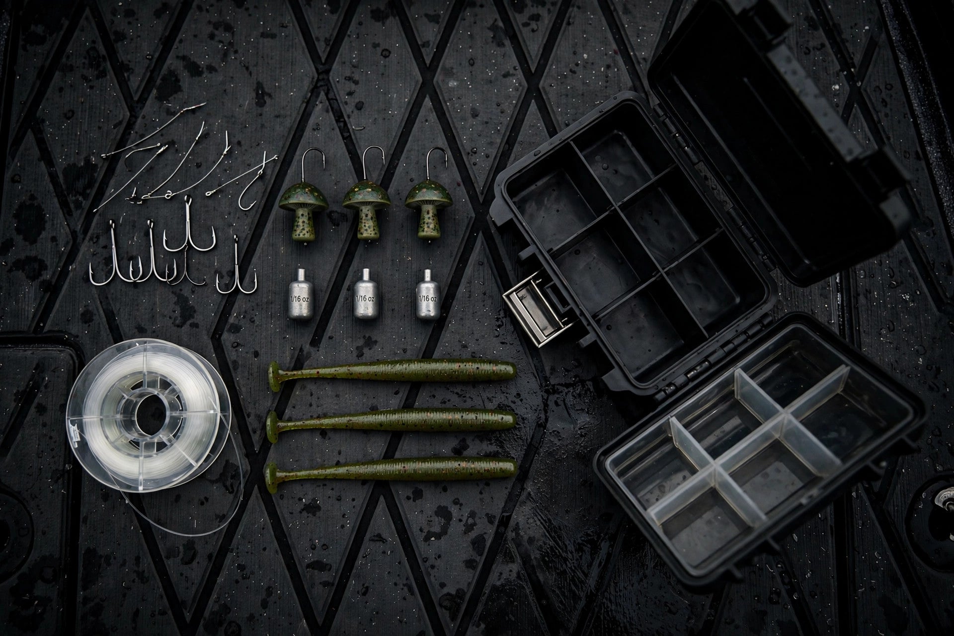Finesse bass tackle flat-lay: hooks, Ned jigheads, drop shot weights, stick worms and fluorocarbon on a dark boat deck