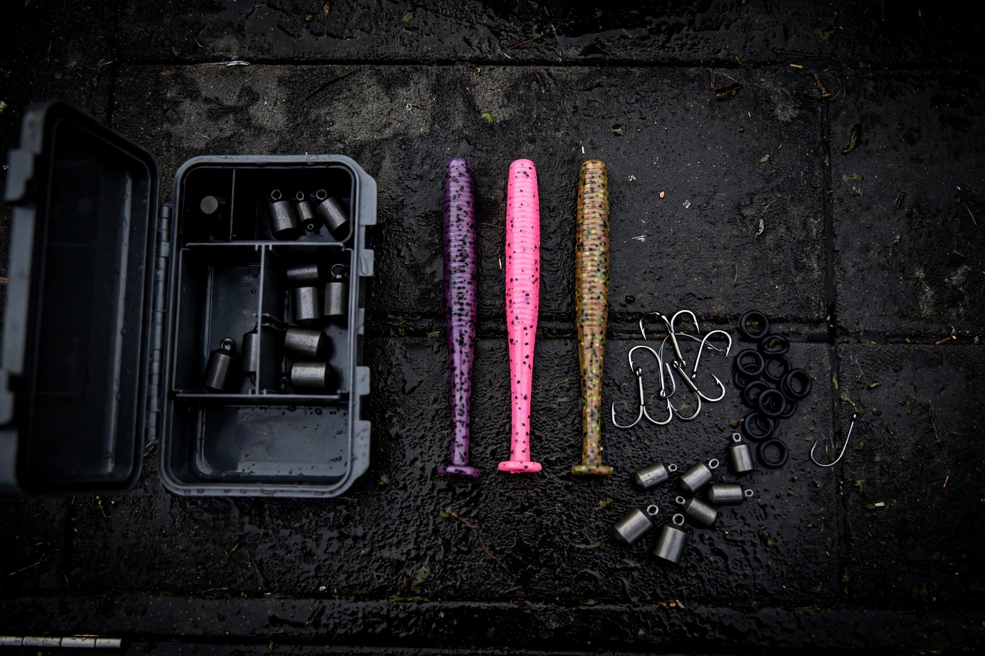 Flat-lay of 4-inch stick worms, wacky hooks, O-rings and tungsten weights on a dark boat deck